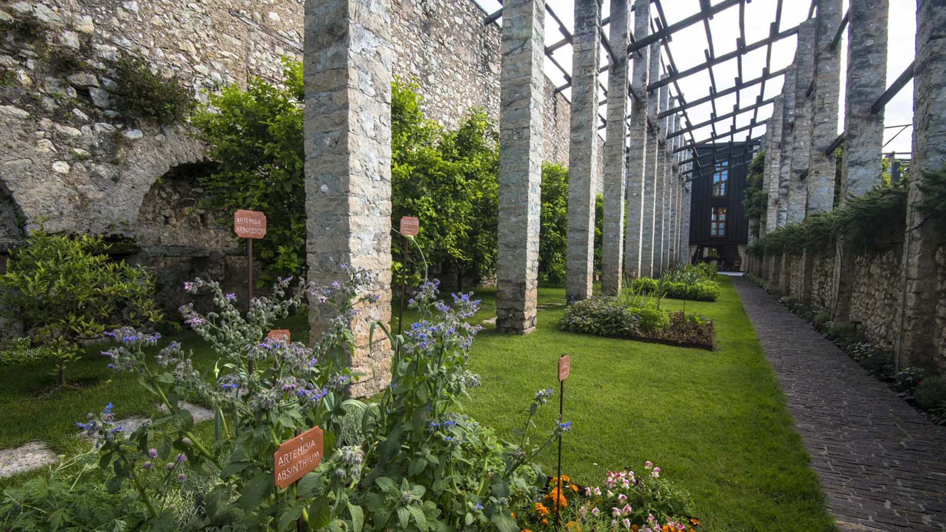 Giardino tra colonne in pietra con lamina corten e vegetazione ordinata