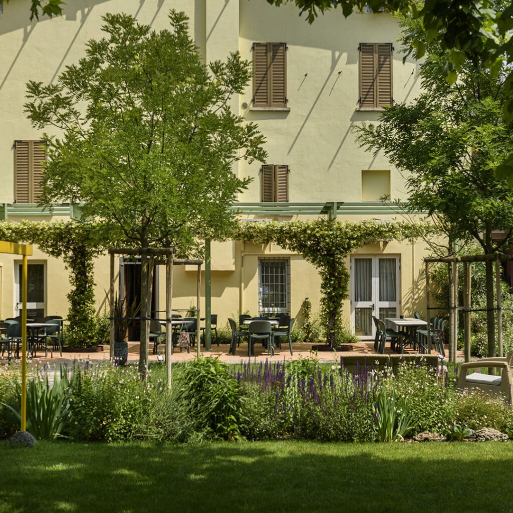 Area attrezzata con tavoli in legno in un giardino pubblico, circondata da prato e alberi