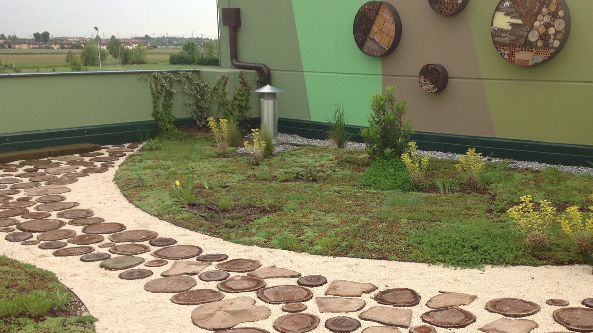 Vialetto in ghiaia e legno su terrazzo verde con aiuole