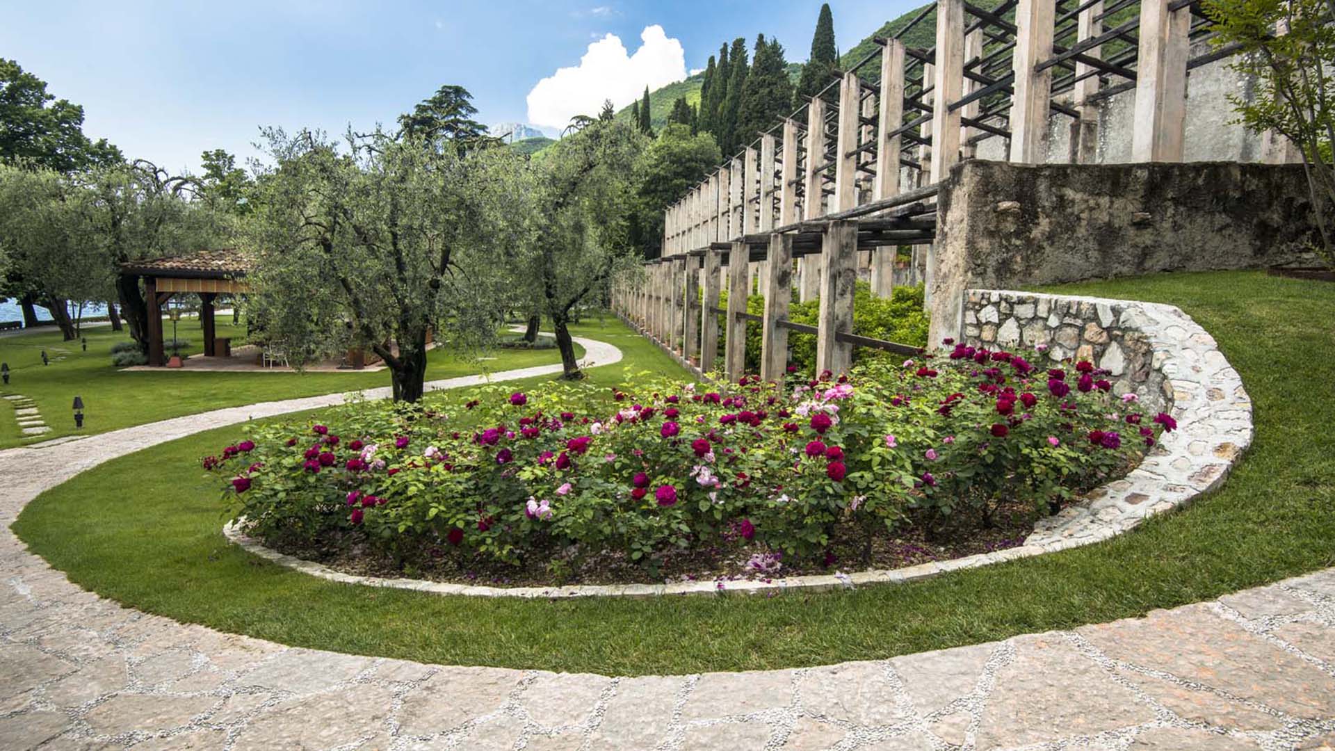 Giardino storico con aiuole fiorite tra ulivi accanto a edificio rurale restaurato a Gargnano